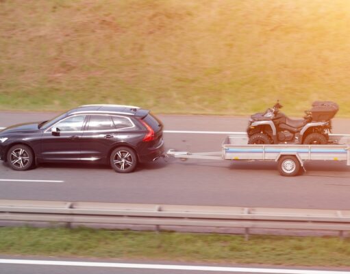 Osobné auto ťahá príves so štvorkolkou počas cestovania