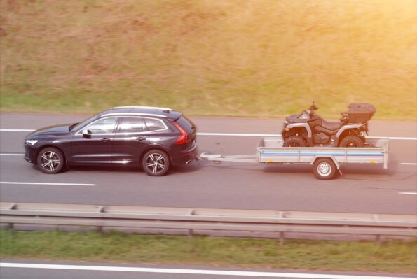 Osobné auto ťahá príves so štvorkolkou počas cestovania